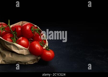 Frische reife rote Tomaten in Papiertüte auf dunklem Hintergrund. Lebensmitteleinkaufkonzept. Platz für Text kopieren Stockfoto