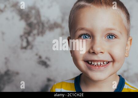 Kleiner Junge posiert vor einer grauen Betonwand. Porträt eines lächelnden Kindes in einem gelb gestreiften T-Shirt Stockfoto