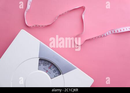 Ein Maßband und Badezimmerwaage auf rosa Hintergrund Stockfoto