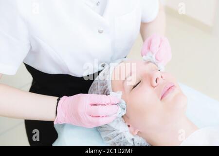 Eine Nahaufnahme des Reinigungsverfahrens im Büro für Kosmetologie. Die Hände des Kosmetologen in rosafarbenen Handschuhen werden gefro entfernt Stockfoto