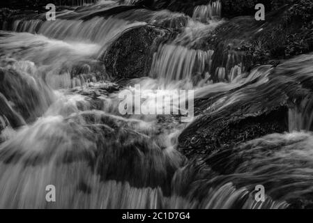Verschwommenes Wasser fließt über moosbedeckten Felsen Stockfoto