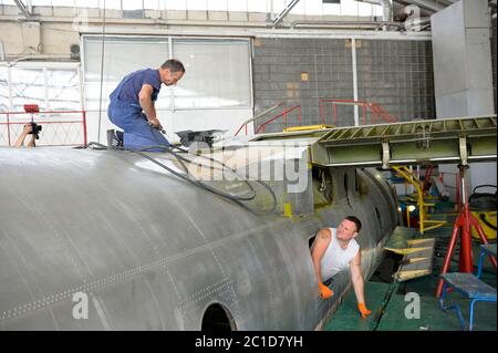 Arbeiter, der mit einem Bohrer in den Händen auf einem Rumpf sitzt, ein anderer, der aus dem Fenster einer Körperebene hängt Stockfoto