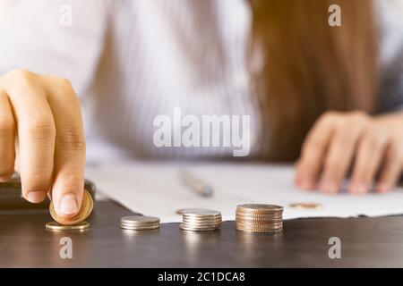 Nahaufnahme der Münzen auf dem Schreibtisch mit einer Geschäftsfrau, die am Schreibtisch arbeitet und eine Münze hält. Ausgaben, Steuern, Haushalt Finanzen Buchführung Konzept. Stockfoto