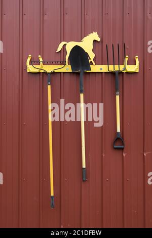 Ein Konzeptfoto eines Rechen, einer Schaufel und einer Pitchfork, die auf einem Gestell hängt. Stockfoto