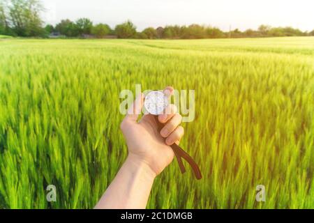 Eine Richtung in der Natur auf einem Weizenfeld finden. Die Hand eines Mannes hält einen Kompass Stockfoto