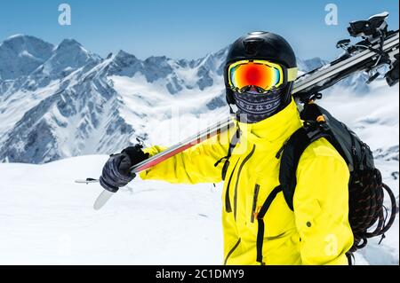 Ein großes Porträt eines Skifahrers in einem Schutzhelm und Brille ist eine Maske und Schal mit Skiern auf der Schulter in der schneebedeckten Stockfoto