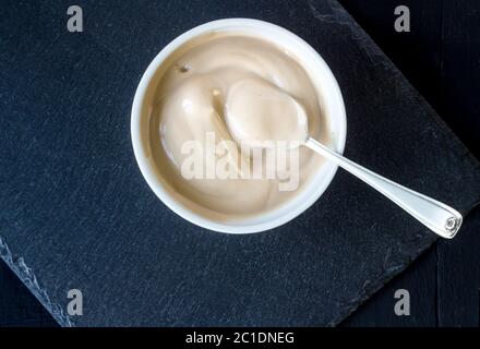 Joghurt in weiße Tasse mit silbernen Löffel auf rustikalen Schiefer schwarzer Hintergrund-cremige Schokolade Joghurt Stockfoto