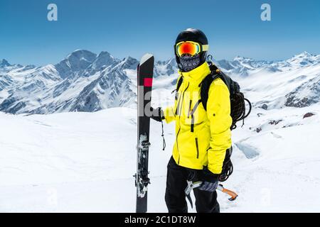 Nahaufnahme eines Skifahrers mit Schutzhelm und Brille. Eine Maske und ein Schal mit einer Eispickel in den Händen neben Skiern Stockfoto