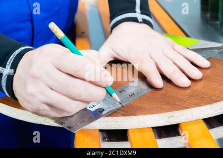 Nahaufnahme der Hand des Zimmermannsmeisters ist mit einem Lineal und einem Bleistiftrohling gekennzeichnet. Das Konzept der manuellen Möbelproduktion Stockfoto