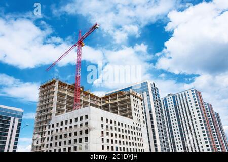 Blick auf ein mehrstöckiges Gebäude im Bau mit hohen Baukräne und einem Glasturm im Hintergrund Wolken blauen Himmel Stockfoto