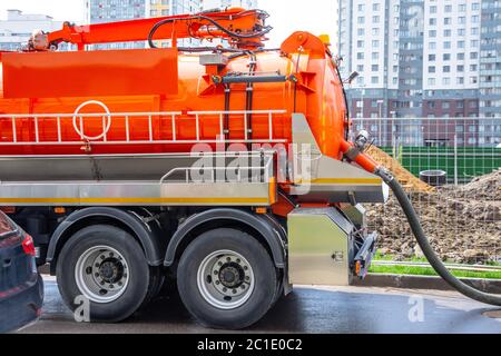 Pumpen von Wasser aus Kanalisation während des Baus von Straßen in der Stadt. LKW mit orangefarbenem Wassertank Stockfoto