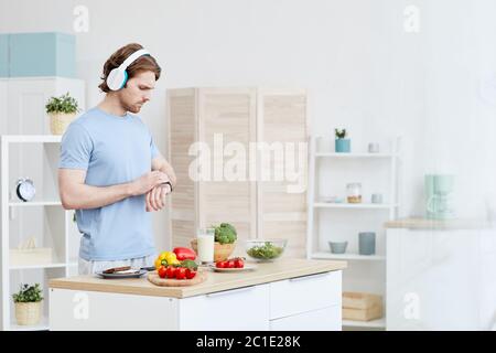 Mann in Kopfhörer Überprüfung der Zeit auf seiner Uhr, während in der Küche steht er gehen, um Abendessen zu machen Stockfoto