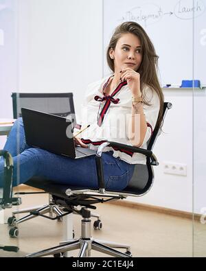 Schöne junge Softwareentwicklerin, die im IT-Büro am Laptop arbeitet, am Tisch im Besprechungsraum eines Softwareentwicklungsunternehmens sitzt oder Stockfoto