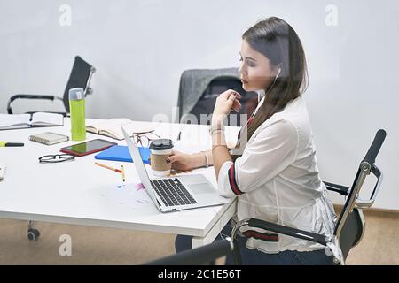 Schöne junge Frau Entwickler oder Manager arbeiten auf Laptop in IT-Büro, sitzen am Tisch im Besprechungsraum eines Software-Entwicklungsunternehmens oder Stockfoto