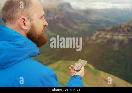 Hipster Mann in einer blauen Jacke mit einem Kompass auf dem Hintergrund im Hintergrund der kaukasischen Landschaft mit einem Plateau Stockfoto