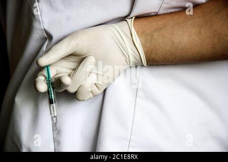Arzt Hand in weißen Handschuh halten Spritze mit Vorbereitungsstrahl von der Nadel. Medizinischer Mann hält Injektor mit Medikamenten in Arm. So Stockfoto