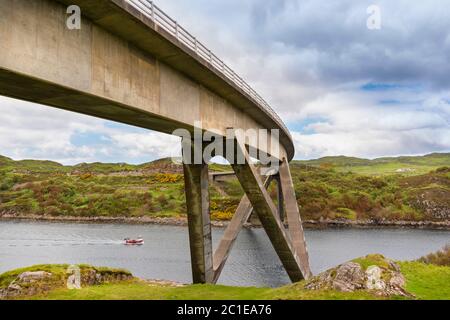 KYLESKU BRÜCKE SUTHERLAND SCHOTTLAND ÜBER LOCH CAIRNBAWN MIT ROTEM FISCHERBOOT, DAS SICH DER BRÜCKE NÄHERT Stockfoto