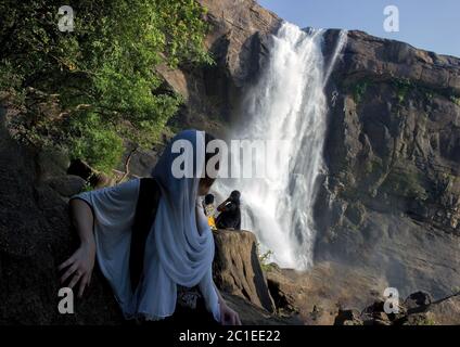 Ein Mädchen in schwarz-weißem Kleid und ein Wasserfall namens Athirapally im Hintergrund in Kerala, Indien Stockfoto