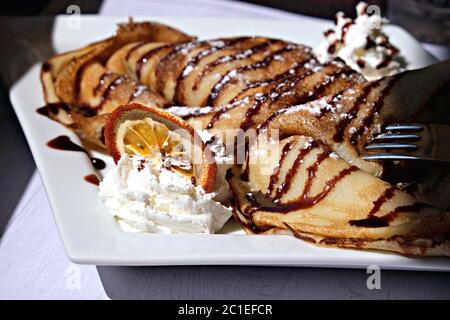 Nahaufnahme von Schokoladenkrepe mit Creme, garniert mit einer Scheibe getrockneter Orange Stockfoto