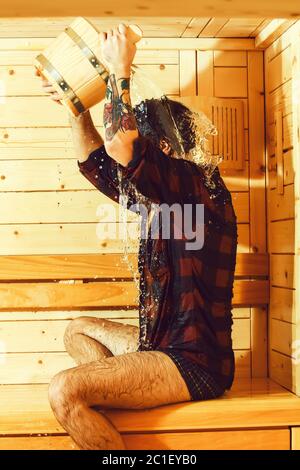 Schöner Mann oder Badende, bärtigen Hipster mit Bart und Schnurrbart in rot kariertem Hemd von der Schaufel gießt Wasser auf dem Kopf in der Sauna, Thermalbad auf hölzernen Hintergrund Stockfoto