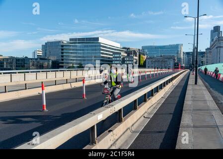 Ein Mann in einer Gesichtsmask fährt ein Santander Leihrad über die London Bridge.Staatssekretär für Verkehr Grant Shapps, Kündigte an, dass alle Passagiere ab dem 15. Juni Gesichtsmasken im öffentlichen Verkehr tragen müssen, und warnte davor, dass das Tragen einer Gesichtsmaske eine Voraussetzung für die Reise ist und dass die Nichteinhaltung zu einer Nichtbeachtung der Flugbedingungen oder einer Geldstrafe führen wird. Stockfoto