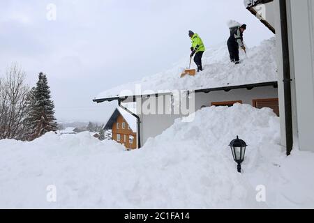 Zwei Männer schaufeln hohen, schweren Schnee von einem Hausdach Stockfoto