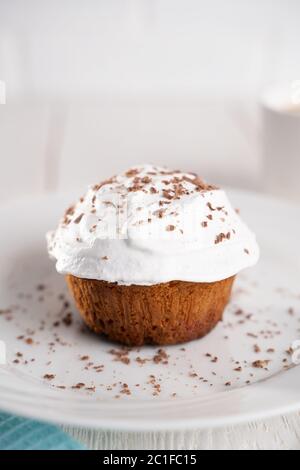 Cupcakes mit Schlagsahne und Schokoladenstückchen auf einem weißen Teller und eine Tasse Kaffee im Hintergrund auf einem weißen Holztisch. Bild für das Menü oder Stockfoto