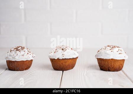 Cupcakes mit Schlagsahne und Schokoladenstückchen auf einem weißen Holztisch. Bild für das Menü oder den Katalog von Süßwaren. Stockfoto