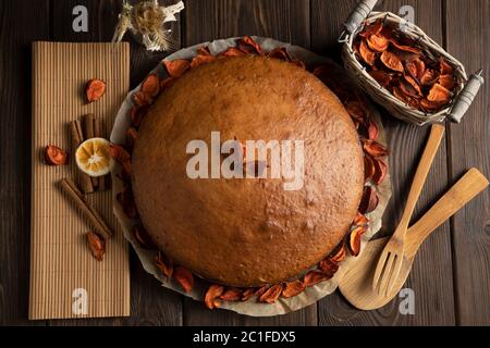 Hausgemachter Kuchen mit getrockneten Blütenblättern auf Pergamentpapier, neben einer Strohserviette, Zimtstangen, Zitrone, Korb und Holzgeräte auf einem dekoriert Stockfoto