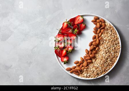 Mit rohen Haferflocken, Mutter und Erdbeere auf grauem Beton Hintergrund Platte. Zutaten für ein gesundes Frühstück top View Stockfoto