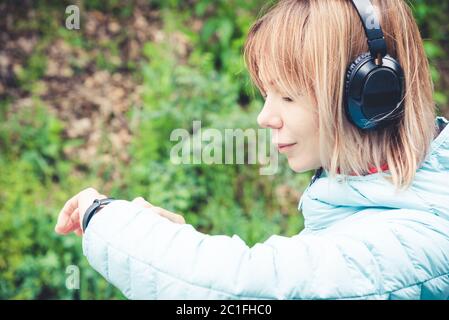Portrait Junge Fitness-Frau schaut auf ihre smarte Uhr, während sie eine Pause vom Sporttraining nimmt. Sportlerin prüft Puls ein Stockfoto
