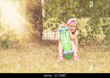 Mädchen mit Skateboard sitzt unter Baum Stockfoto