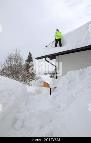 Ein Mann schaufelt hohen, schweren Schnee von einem Hausdach Stockfoto