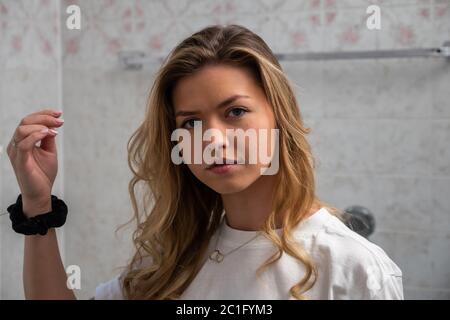 Ziemlich blonde Frau, die Kamera vor der Fixierung Haare in zu Hause Bad. Nahaufnahme. Stockfoto