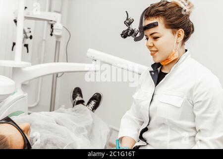 Zahnarzt junge Frau behandelt einen Patienten einen Mann. Der Arzt verwendet Einweghandschuhe, eine Maske und einen Hut. Der Zahnarzt arbeitet im Mund des Patienten, verwendet ein Stockfoto