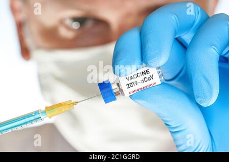 Hand in blauen Handschuh halten kleine Fläschchen mit Coronavirus-Impfstoff (Label eigenes Design, nicht echtes Produkt), um es mit hypodermischen Spritze Nadel, blu injizieren Stockfoto