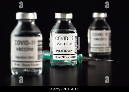 Coronavirus Covid-19 Impfstoffkonzept - drei Glasfläschchen auf schwarzem Tisch, hypodermische Spritzennadel in der Nähe, Nahaufnahme Detail (Label eigenes Design - Dummy dat Stockfoto