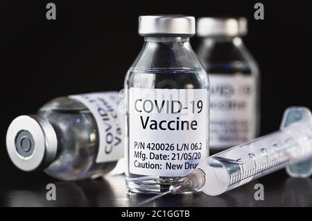 Coronavirus Covid-19 Impfstoffkonzept - drei Glasfläschchen auf schwarzem Tisch, hypodermische Spritzennadel in der Nähe, Nahaufnahme Detail (Label eigenes Design - Dummy dat Stockfoto