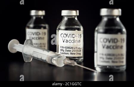 Coronavirus Covid-19 Impfstoffkonzept - drei Glasfläschchen auf schwarzem Tisch, hypodermische Spritzennadel in der Nähe, Nahaufnahme Detail (Label eigenes Design - Dummy dat Stockfoto