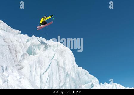 Ein springender Skifahrer, der von einem Gletscher gegen einen blauen Himmel hoch in den Bergen springt. Professionelles Skifahren Stockfoto