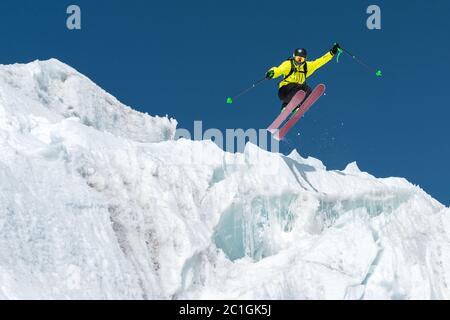 Ein springender Skifahrer, der von einem Gletscher gegen einen blauen Himmel hoch in den Bergen springt. Professionelles Skifahren Stockfoto