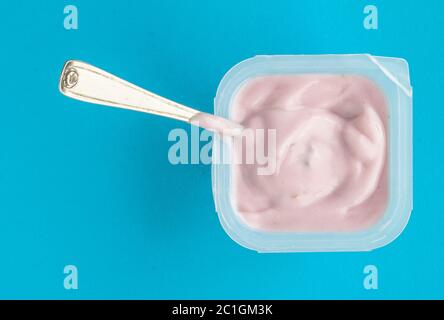 Joghurt im Becher close up-Rosa Joghurt auf blauem Hintergrund mit kleinen silbernen Löffel Stockfoto