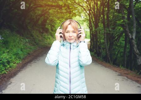 Portrait einer schönen jungen Frau, die Kopfhörer hält und Musik im Freien im Wald hört. Fröhliche Musik Stockfoto