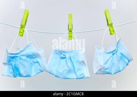Gebrauchte Einweg-Schutz chirurgische Masken Trocknen auf einer Wäscheleine mit grünen Wäscheklammern auf weißem Hintergrund. Stockfoto