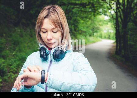 Portrait Junge Fitness-Frau schaut auf ihre smarte Uhr, während sie eine Pause vom Sporttraining nimmt. Sportlerin prüft Puls ein Stockfoto
