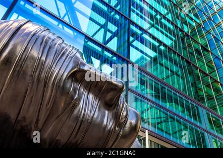 Nahaufnahme der Skulptur eines Kopfes von Igor Mitoraj 'Testa Addormentata' (1983) gegen das zeitgenössische Glasgebäude, Canary Wharf, London, Großbritannien Stockfoto