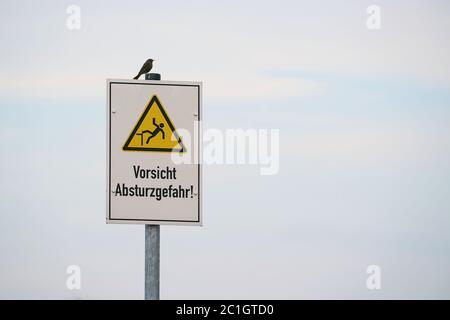 Schild mit der Aufschrift 'Vorsicht, Fallgefahr'. Auf dem Schild sitzt ein Vogel. Stockfoto