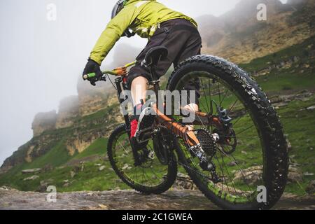 Beine von Radfahrer und Hinterrad Nahaufnahme des hinteren mtb-Bikes in den Bergen vor dem Hintergrund von Felsen bei nebligen Wetter. Die c Stockfoto