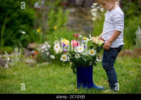 Kind hält Gummistiefel mit schönen Blumen im Garten Stockfoto