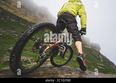 Beine von Radfahrer und Hinterrad Nahaufnahme des hinteren mtb-Bikes in den Bergen vor dem Hintergrund von Felsen bei nebligen Wetter. Die c Stockfoto